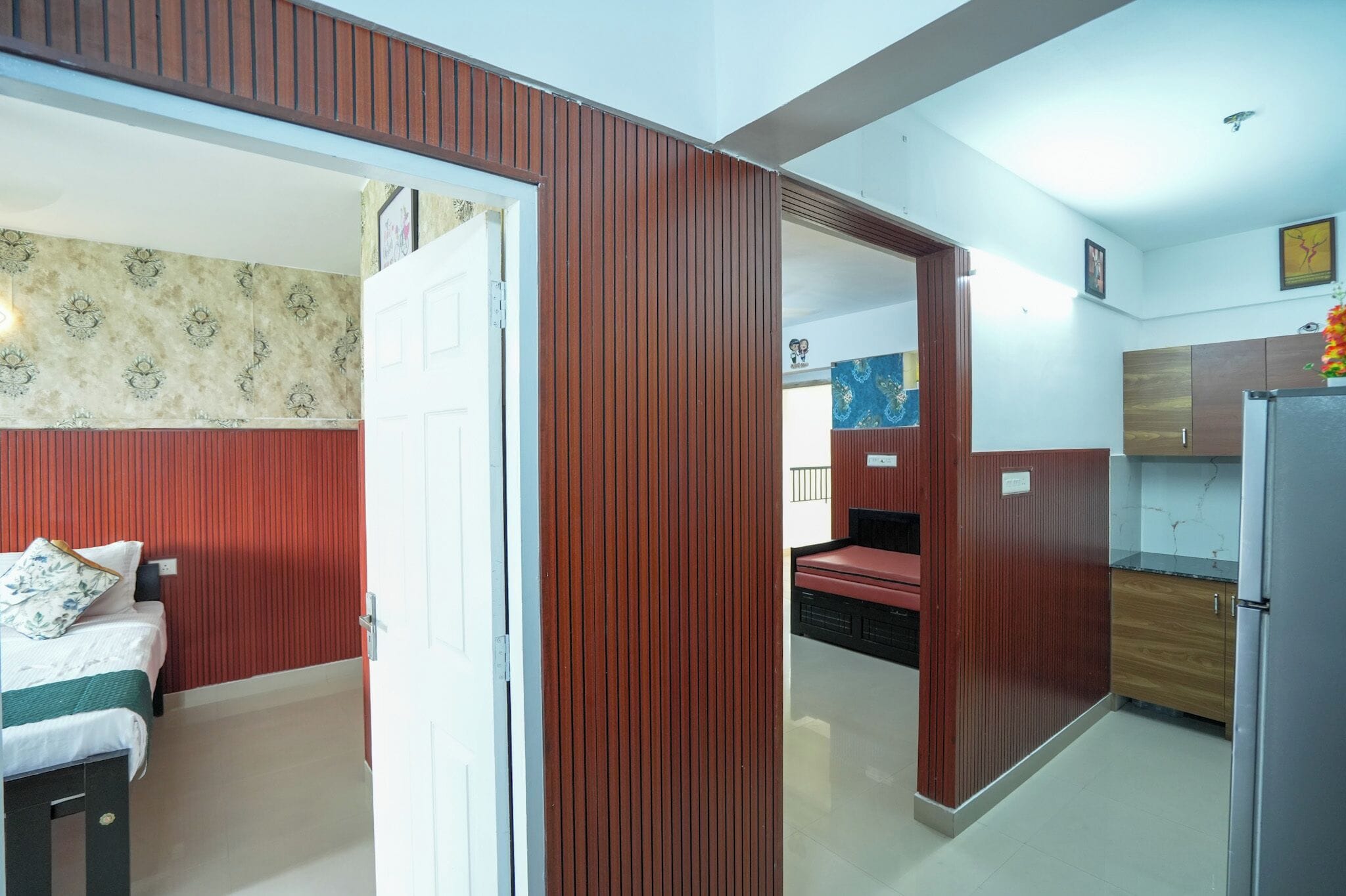 Una habitación con cama, puerta de madera, zona de cocina con armarios y baño con inodoro y lavabo.