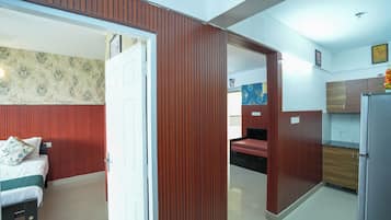 Una habitación con cama, puerta de madera, zona de cocina con armarios y baño con inodoro y lavabo.
