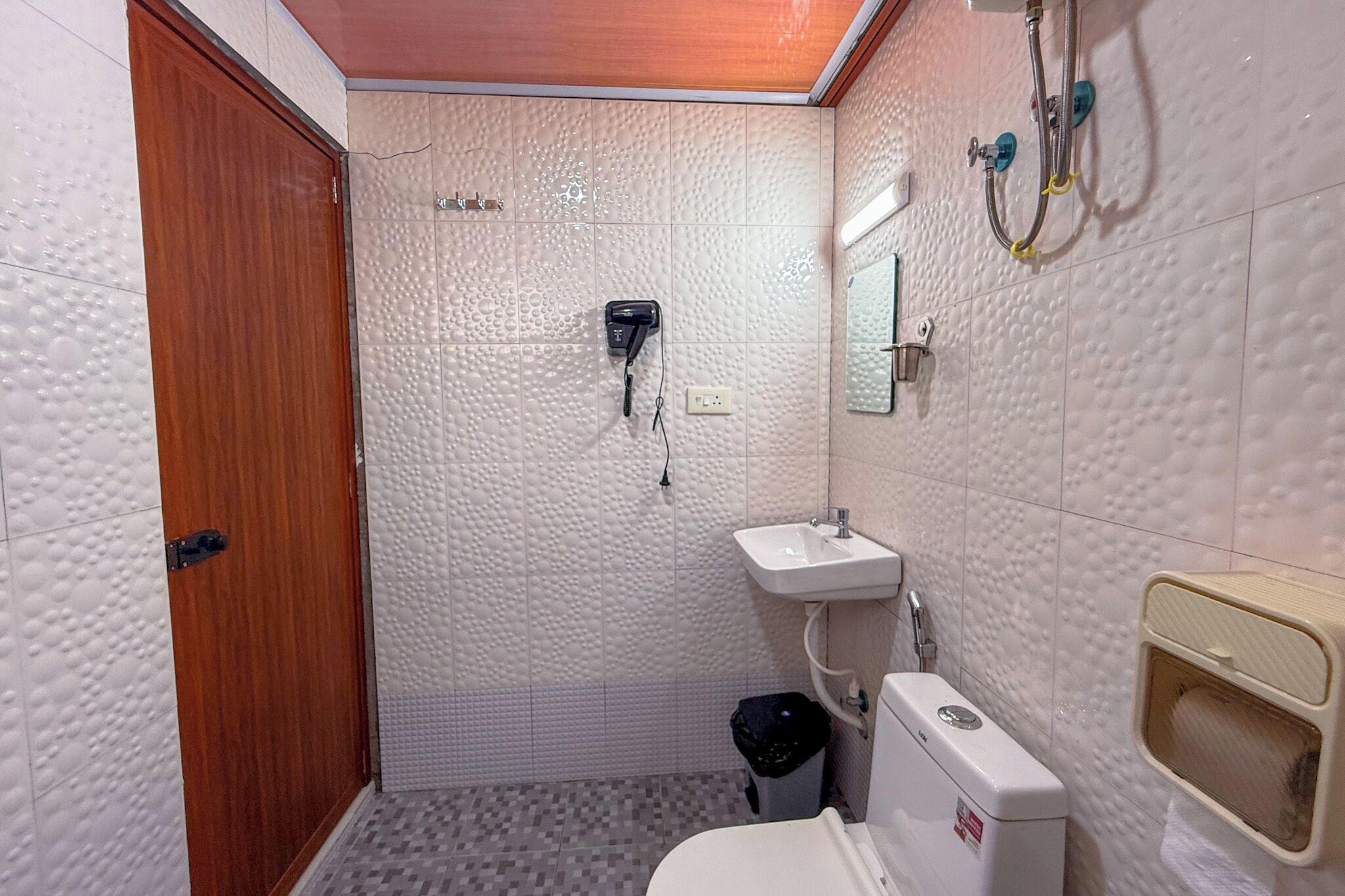 Un baño pequeño con puerta de madera, dispensador de toallas, inodoro y zona de ducha.