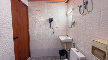 Un baño pequeño con puerta de madera, dispensador de toallas, inodoro y zona de ducha.
