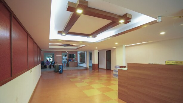 A spacious lobby with a checkered floor, a reception desk, and a high ceiling with exposed beams and recessed lighting. - Sancta Monica Lounge -Cochin Airport  (Nedumbassery)
