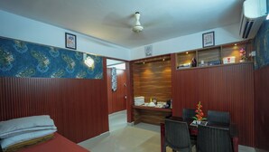 A hotel room with a bed, a dining table with chairs, a wooden cabinet, and a wall with a blue floral pattern. - Sancta Monica Lounge -Cochin Airport  (Nedumbassery)