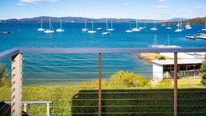 A marina with multiple sailboats docked, a grassy area with a small building, and a clear view of the water and distant hills. - StayAU · The River House · Paradise Pet-friendly (Beauty Point)