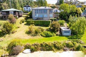 Une maison à deux étages, dotée d’un toit plat et de grandes fenêtres, entourée d’un jardin bien entretenu et d’un petit abri de jardin.