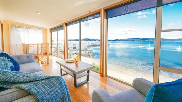 A spacious living room with a large window offering a view of the sea and boats. - StayAU · The River House · Paradise Pet-friendly (Beauty Point)