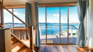A spacious room with a large sliding glass door leading to a balcony with a view of the sea and a bridge. - StayAU · The River House · Paradise Pet-friendly (Beauty Point)