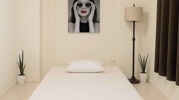 A minimalist bedroom with a single bed, a wall-mounted air vent, a floor lamp, and two potted plants.