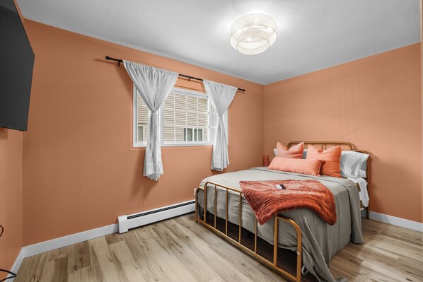 Een slaapkamer met een bed, gordijnen, een plafondlamp en een radiator.