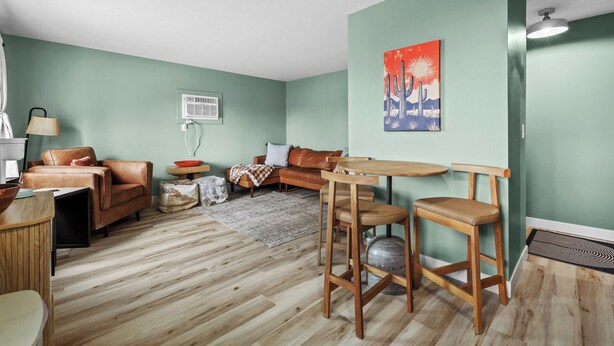 A living room with a wooden floor, a brown leather sofa, a wooden coffee table, and a painting of a desert scene. - Cozy 2 Bedroom Apartment within walking distance from the Hospital. (Williston)