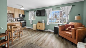 A compact living space with a kitchenette, a sofa, a dining area, and a large window providing natural light. - Cozy 2 Bedroom Apartment within walking distance from the Hospital. (Williston)