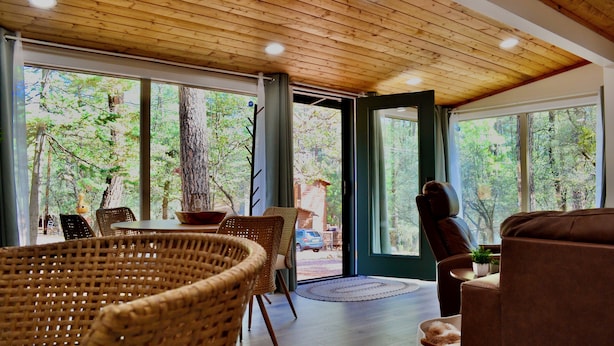 Una habitación con techo de madera, ventanas amplias, mobiliario de mimbre y un sofá marrón.