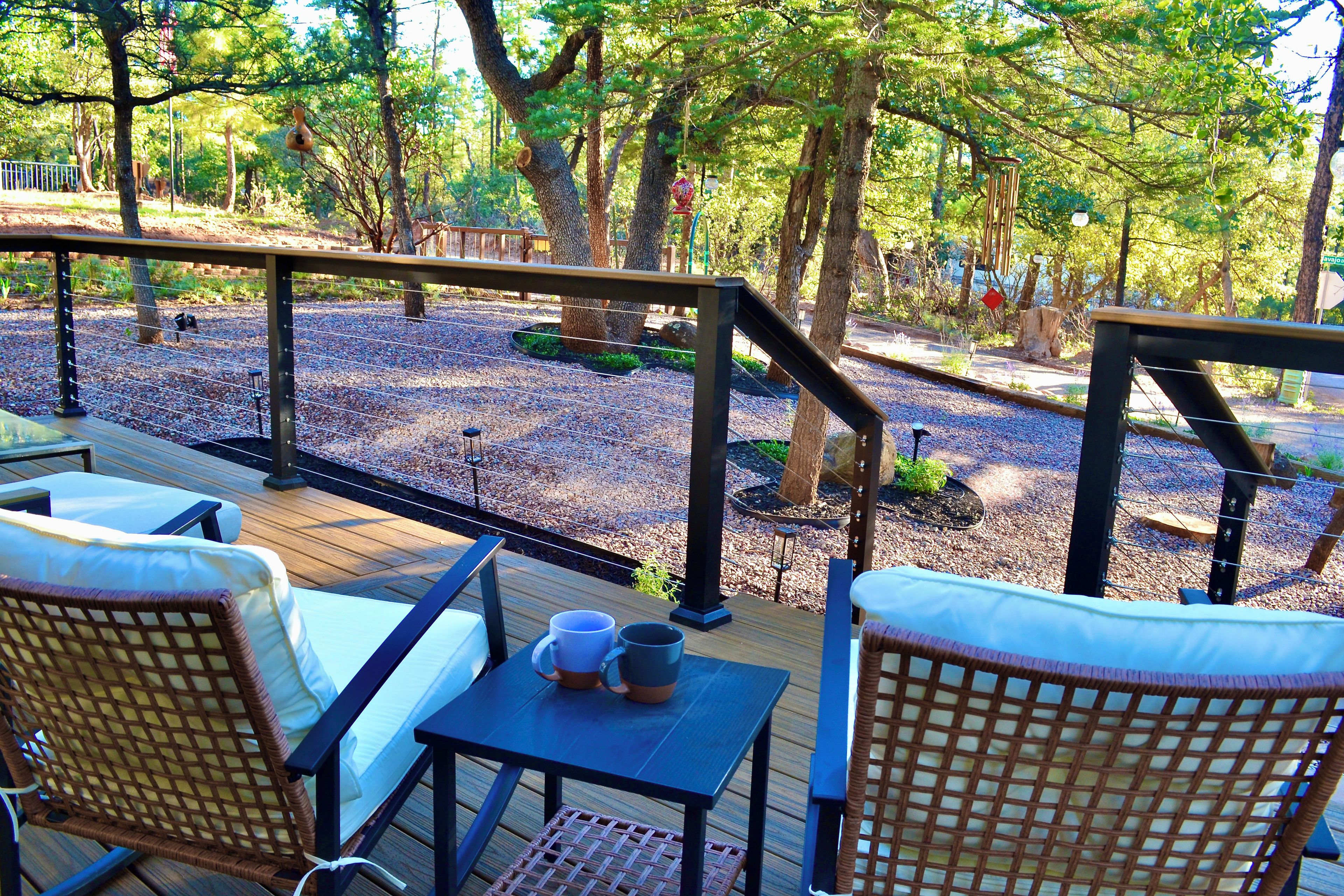 A deck with wicker furniture and a table, overlooking a gravel area with trees.