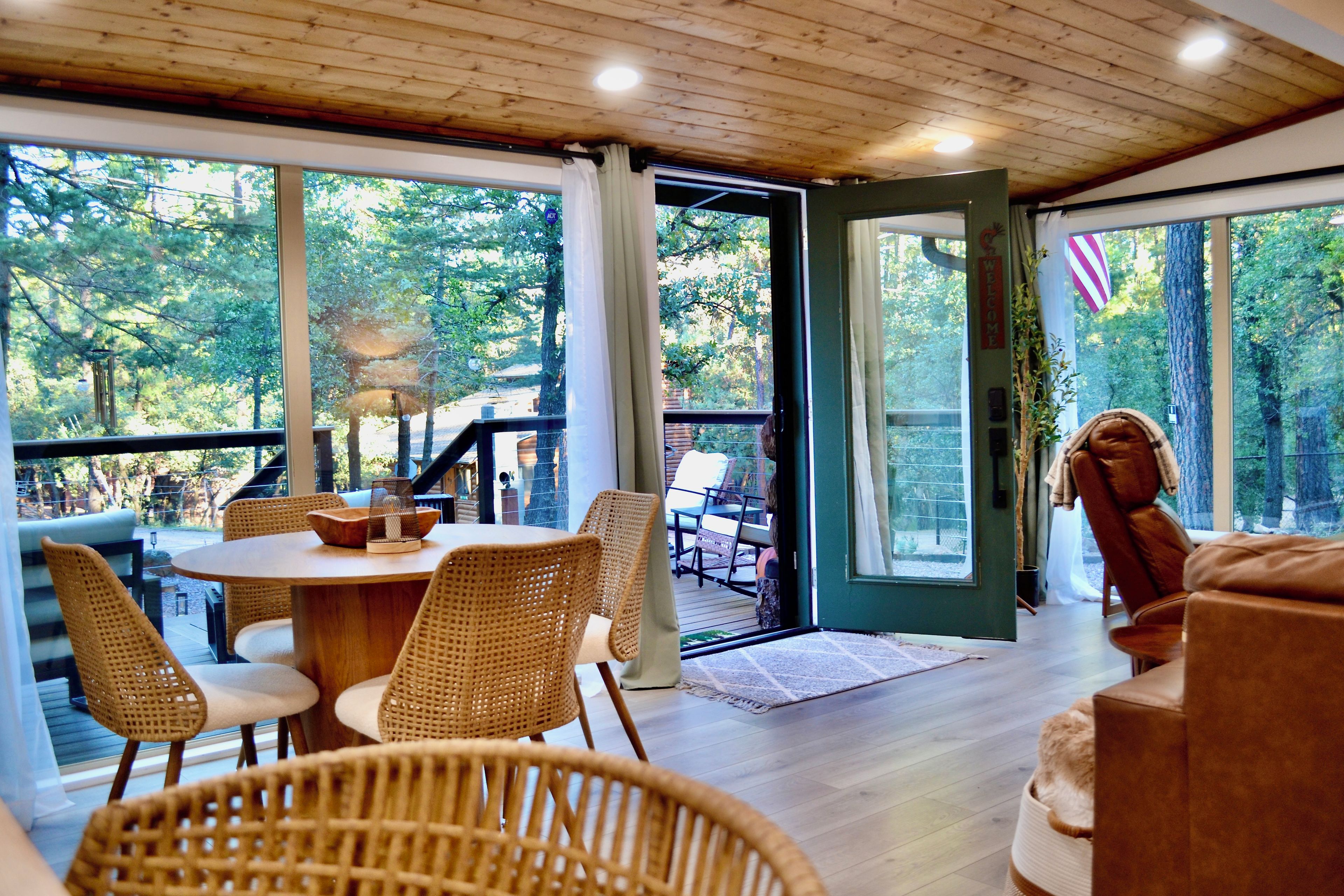 A wooden deck with outdoor seating, large windows, and a view of trees.