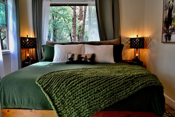 Un dormitorio con una cama grande, dos lámparas de noche, una ventana con cortinas y un cuadro en la pared.