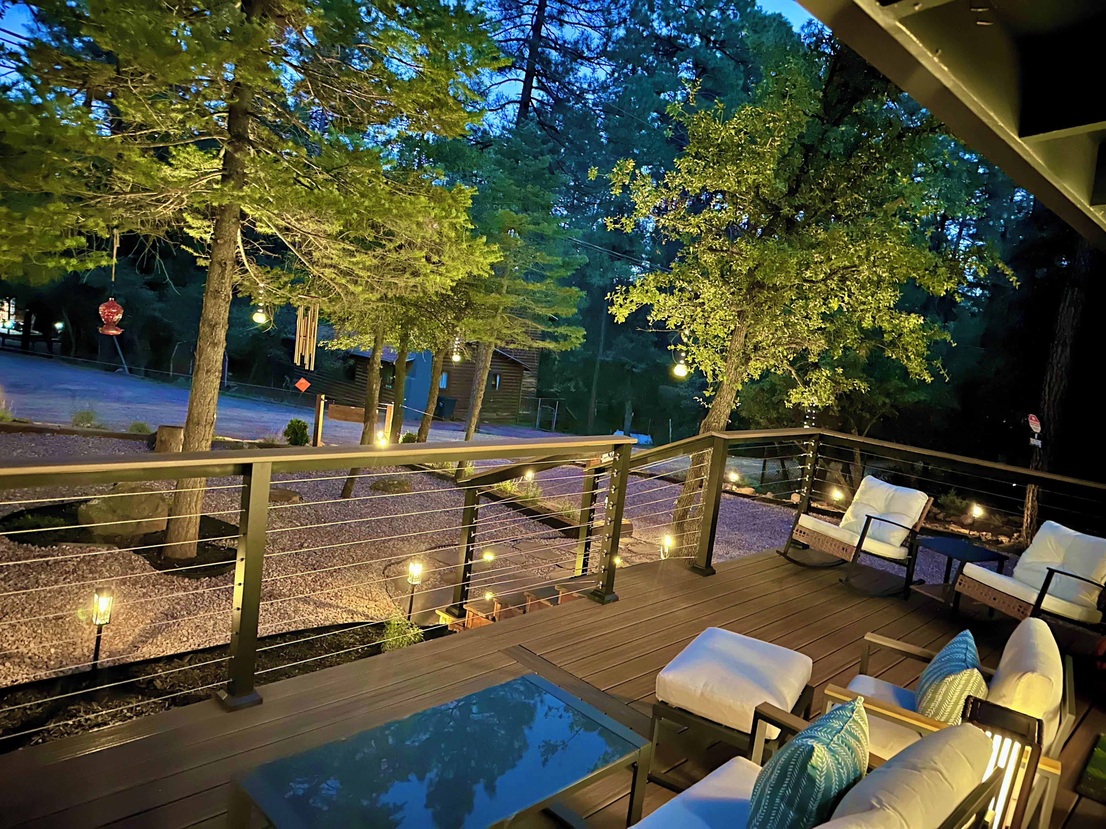 A deck with outdoor seating and a pool, surrounded by trees and a wooden fence.
