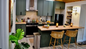 Una cocina moderna con gabinetes verdes, una isla de madera y dos taburetes de mimbre.