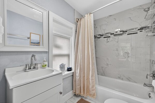 Une salle de bain avec un meuble-lavabo blanc, une douche avec un mur en marbre et une baignoire.