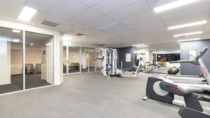 A modern gym with exercise equipment, glass walls, and a grey carpeted floor. - 
Central Emporium | Hotel-Style 1BR w/ King Bed (Melbourne)