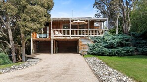 Une maison en bois à deux étages, dotée d’un balcon, d’un garage et d’une allée gravillonnée.