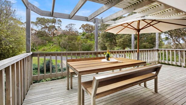 Une terrasse en bois avec une table et un banc, un parasol et une bouteille de champagne.