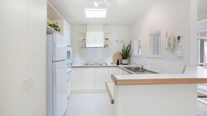Une cuisine moderne avec des meubles blancs, un four encastré, un évier et un petit îlot central doté d’un plan de travail en bois.