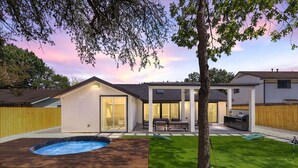 Ein modernes Haus mit Swimmingpool, einer Terrasse mit Gartenmöbeln und einem gepflegten Rasen.