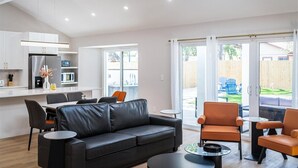 Ein zeitgem äßer Wohnraum mit einem schwarzen Ledersofa, orangefarbenen Sesseln, einem Essbereich und einer Küche.