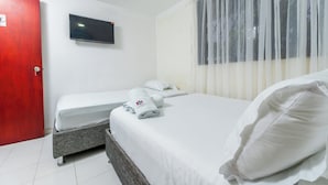Een hotelkamer met een bed, een televisie en een raam met dunne gordijnen.