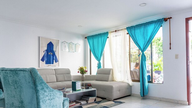 Een woonkamer met een bank, een blauwgroene fauteuil, een salontafel met boeken en een raam met gordijnen.