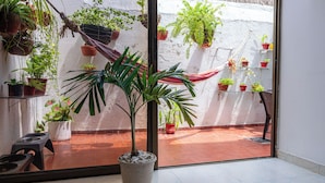 Een kamer met een groot raam, potplanten, een hangmat en een betegelde vloer.