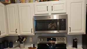 A kitchen with white cabinets, a stainless steel microwave, a stove, and a coffee maker.
