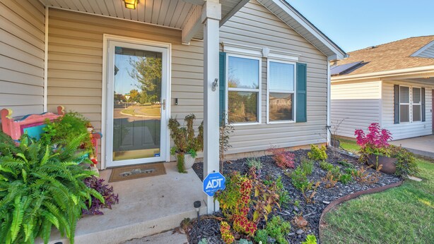 A house with a front porch, a door, and a small garden with various plants.