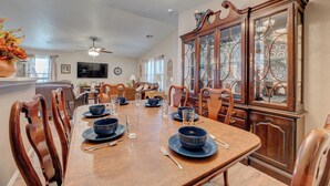 A dining room with a wooden table set for four, surrounded by wooden chairs. A large wooden cabinet with glass doors is to the right.