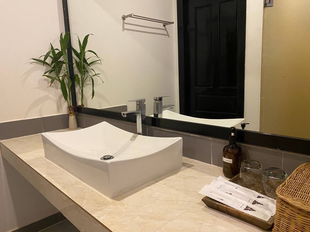 A bathroom with a white sink, a mirror, a towel rack, a potted plant, and a bottle of hand soap.