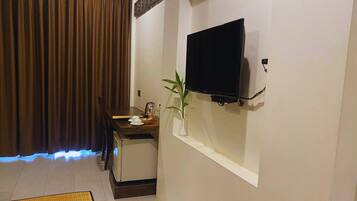A small room with a TV mounted on the wall, a desk with a plant, and a dining table.