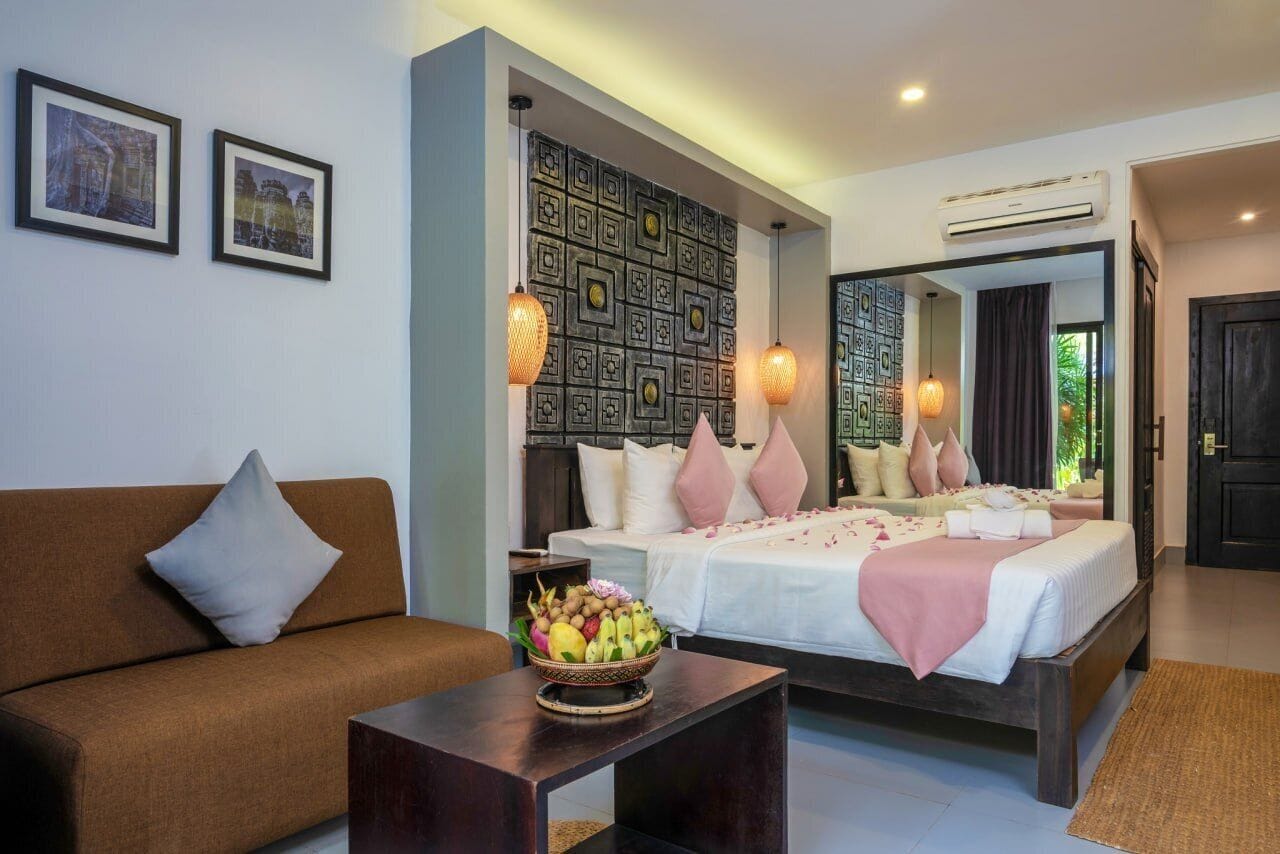 Quarto moderno com cama grande, sofá, mesinha com uma cesta de frutas e um painel decorativo na parede.