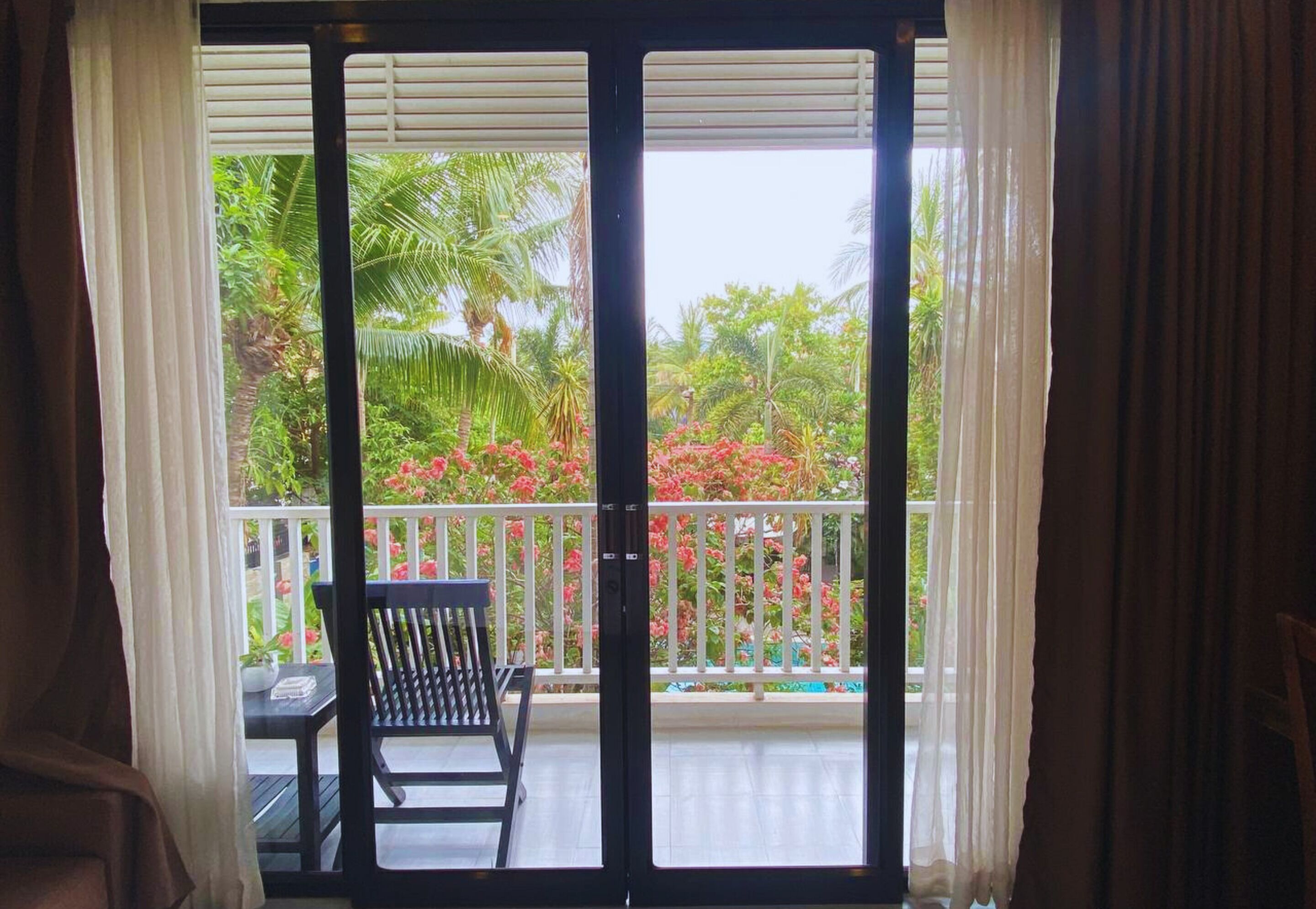 A balcony with a chair and a table, overlooking a garden with various plants and flowers.