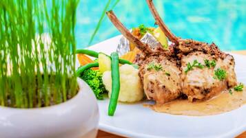 A plate of food with lamb chops, vegetables, and a creamy sauce.
