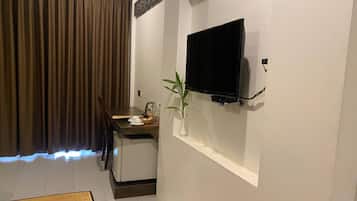 A compact living space with a television mounted on the wall, a small dining table, a refrigerator, and a decorative plant.