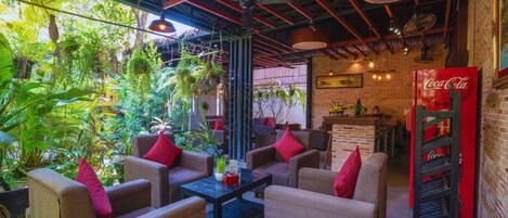 A cozy indoor seating area with sofas and a coffee table, surrounded by lush greenery and a brick wall.