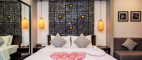 A hotel room with a bed, a headboard with a decorative pattern, two bedside lamps, a sofa, and a mirror.