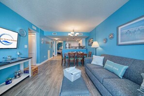Ein Wohnzimmer mit einem blauen Sofa, einem Esstisch und einer Küche im Hintergrund.