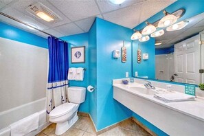 Een badkamer met een blauwe accentmuur, een wit toilet, een blauw douchegordijn en een wastafel met een spiegel erboven.