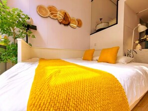 Une chambre à coucher avec un lit, un plaid jaune et une œuvre d’art en bois accrochée au mur.