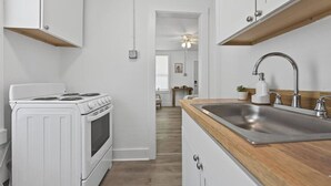 Eine schmale Küche mit weißen Schränken, einem Herd und einer Holz Arbeitsplatte mit Spüle.