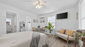 Ein modernes Schlafzimmer mit einem großen Bett, einem Deckenventilator, einem Fernseher, einer Sitzecke und einem Essbereich.