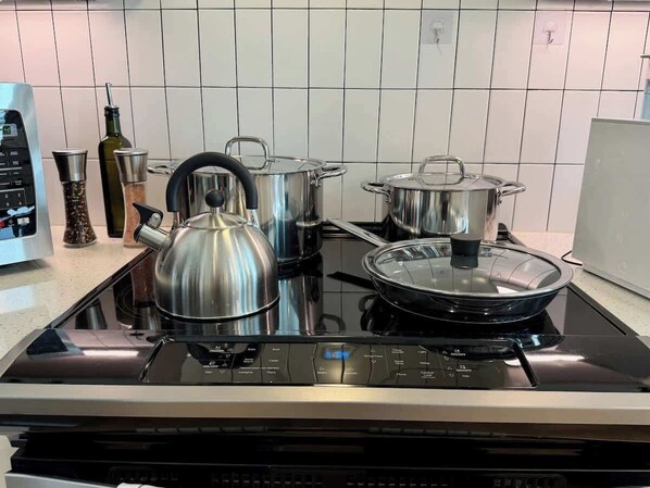 A kitchen with a black induction cooktop, stainless steel pots, a kettle, and a bottle of olive oil.