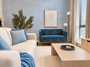 A modern living room with a sofa, a blue armchair, a coffee table, a floor lamp, and a framed artwork on the wall.