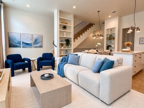 A modern living room with a sofa, two armchairs, a coffee table, and a staircase leading to a dining area.