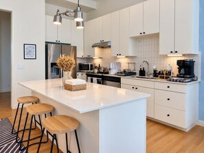 A modern kitchen with white cabinetry, stainless steel appliances, and a central island with stools.